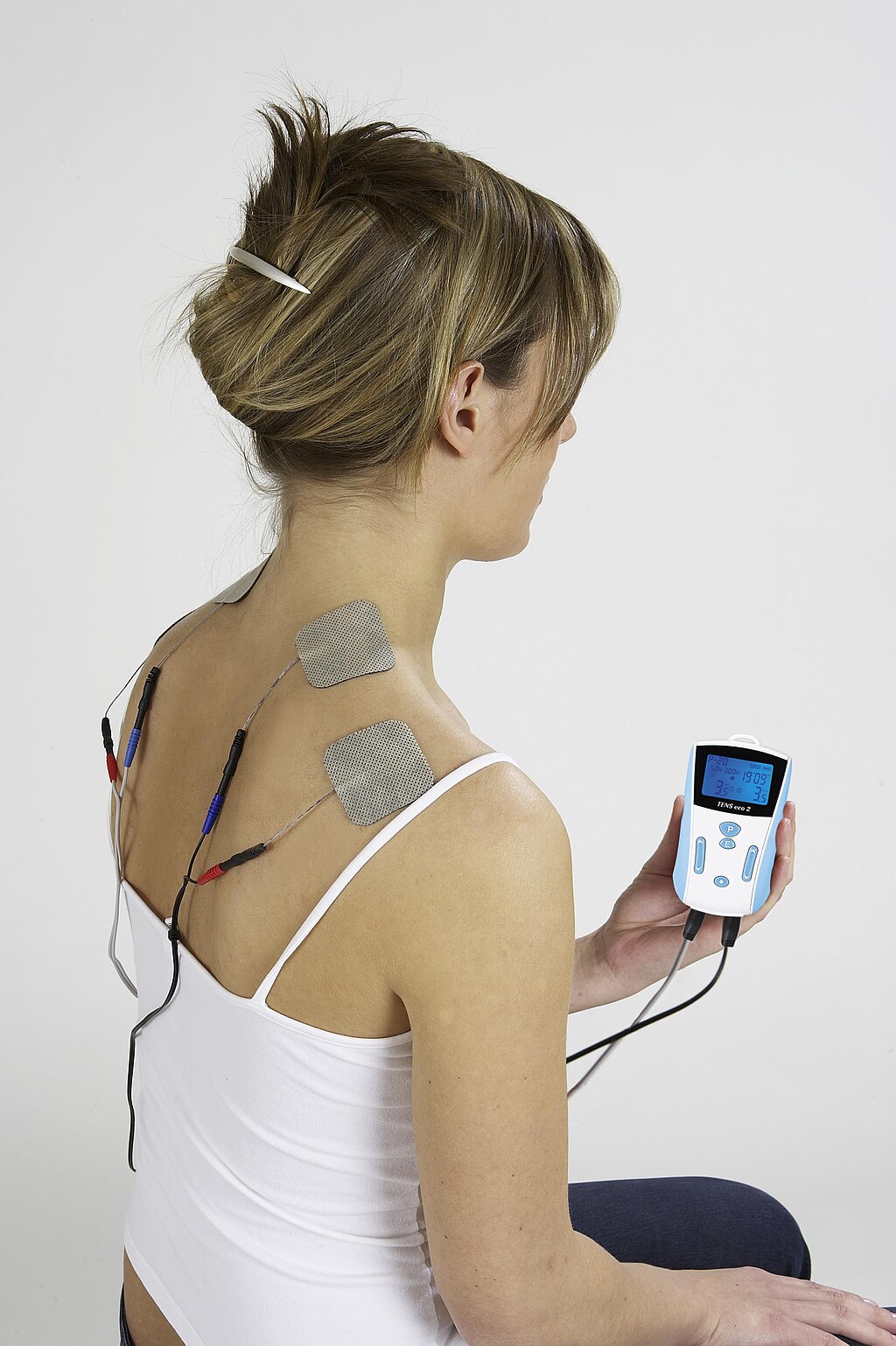 Ervaring TENS bij RSI-klachten: vrouw met opgeplakte elektroden in de nek, met een werkend TENS-apparaat